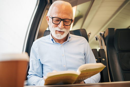 Elderly gray-haired man reading a paper book while sitting on a train
