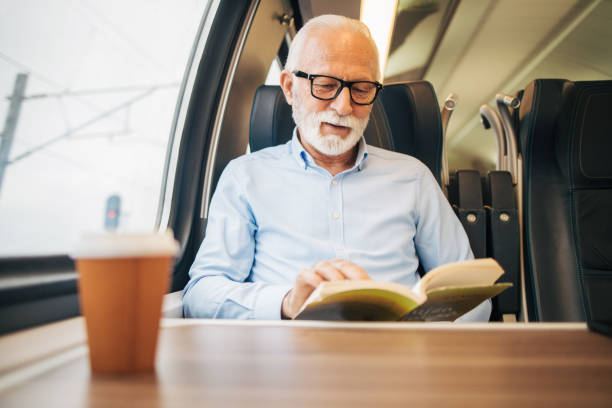 istock Elderly gray-haired man reading a paper book while sitting on a train 1964300826