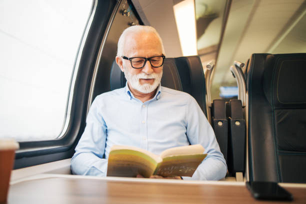 istock Elderly gray-haired man reading a paper book while sitting on a train 1964300835