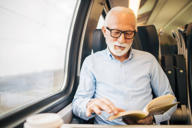 istock Elderly gray-haired man reading a paper book while sitting on a train 1964300836