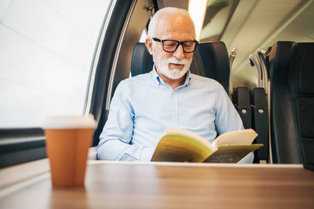istock Elderly gray-haired man reading a paper book while sitting on a train 1964300837