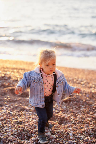 istock Little girl in a jacket walks along a pebble beach 1964301373