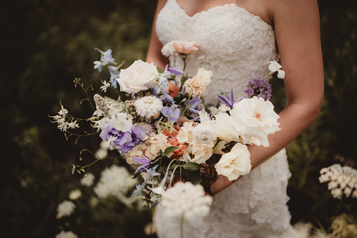 Bride in lace wedding dress holding light colored wedding bouquet