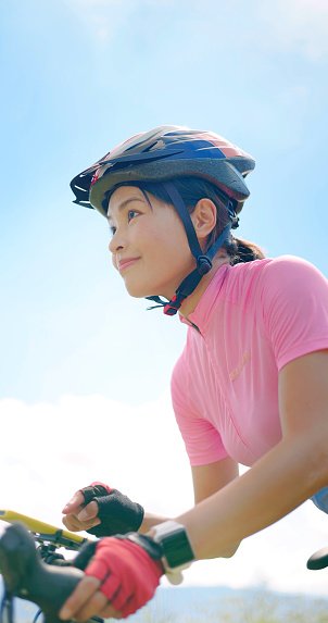enjoy sport or healthy lifestyle concept - asian young woman wearing helmet is setting tracker app through mobile phone and smart watch while standing by a bicycle on the road