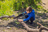 A boy scout saws tree branches for a fire in the forest. Scout camp. Preparing to lighting a fire. Preparation of firewood logs for the fire. Axes and saws. Scout and touristic equipment. Tools