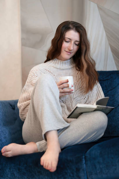 istock Young woman reading book at home 1964464585