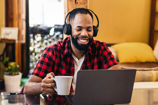 Smiling black man working remotely from home with laptop computer and headphones. Telecommuting and home office concept.