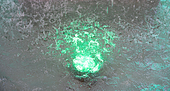 The splashing water surface below has a green light, the image looks blurry to show the movement.