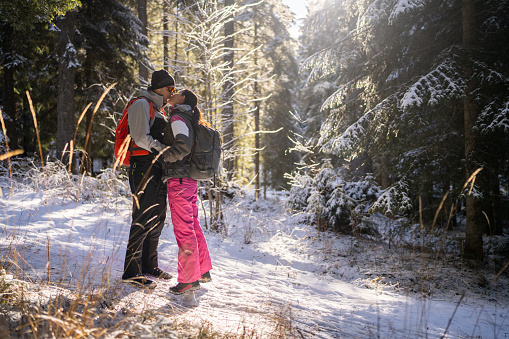 Full length shot of couple in love kissing in snowy forest on their winter vacation