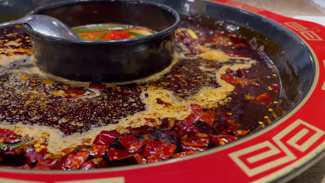 Close up of Sichuan Hotpot slowly boiling as red hot chilli peppers swim across the spicy soup