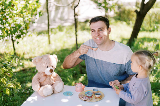 テディベアとテーブルでおもちゃのカップで笑顔のお父さんを見ている小さな女の子 - tea party little girls teapot child ストックフォトと画像