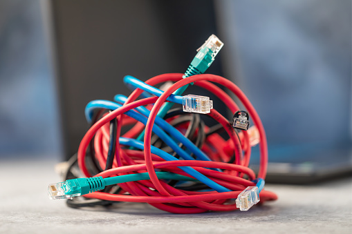A bunch of network computer wires tangled together on the background of a laptop, a concept on the topic of difficulty when connecting to a local network or the Internet via a wire