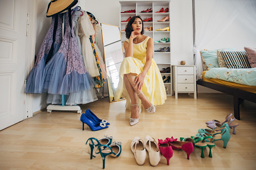 Classy young woman choosing shoes in her bedroom at home.