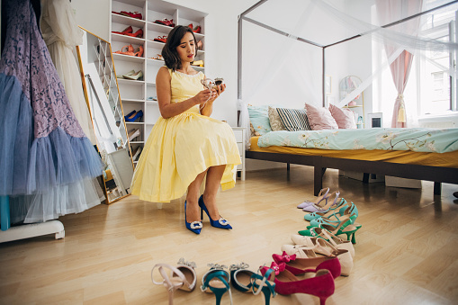 Classy young woman choosing shoes in her bedroom at home.
