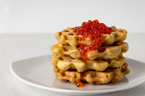 Viennese waffles with red caviar lie in a stack on a white plate, copy space
