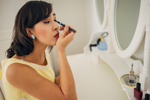 Classy young woman applying make up on face in her apartment.