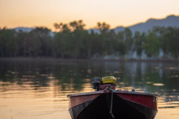 Boat drifts peacefully on serene river beneath golden sunset, reflecting tranquil nature
