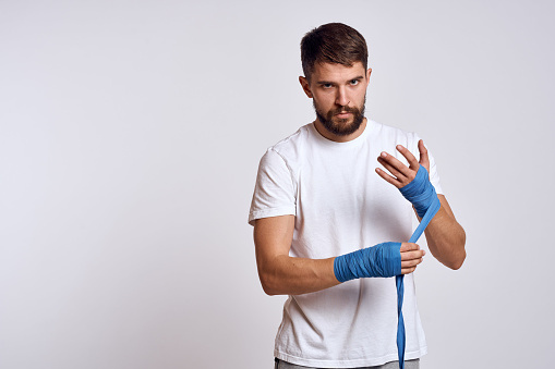 sports man in white t-shirt blue boxing bandages on his arms workout exercises. High quality photo