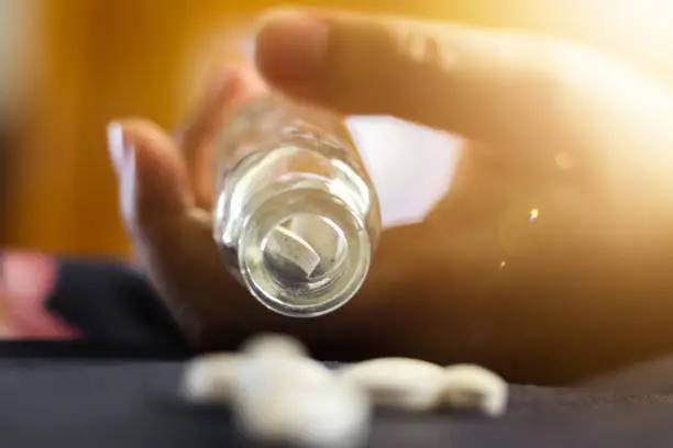 Photo of person's hand holding a medicine bottle with pills, contraceptive overdose