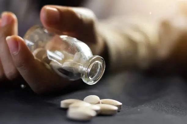 Photo of person's hand holding a medicine bottle with pills, contraceptive overdose