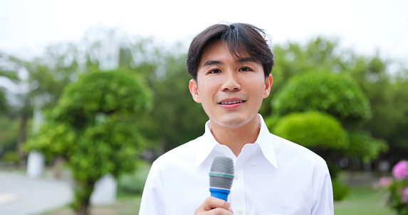 close up portrait asian male reporter standing at park in city has live broadcast