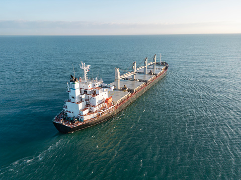 The tug accompanies the ship when entering the cargo port. Aerial drone view above sea port. Cargo vessel is loading containers and bulk. Professional business logistics and transportation of cargo ship.