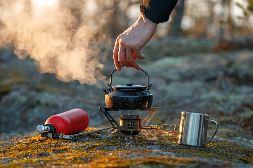 A man brews delicious tea in a kettle on a gasoline burner in the autumn forest.