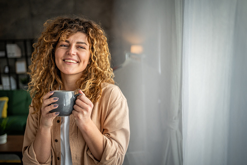 Beautiful attractive young woman enjoying her morning coffee at home, sitting by the window
