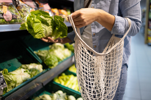 An unrecognizable woman is using an eco-friendly string bag for her salad ingredients in a supermarket
