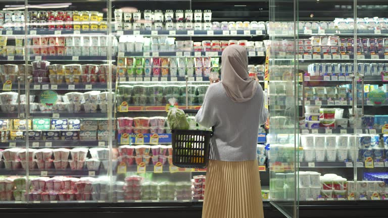 Rear View Of Muslim Woman Shopping Groceries Products From Refrigerated Section In Supermarket