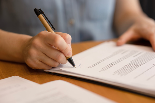 A woman's hand signs documents with a pen, close-up. A woman works with business documents, signs a lease agreement or a contract