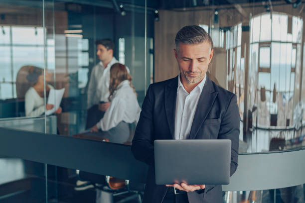 istock Focused male manager working on laptop while standing in modern office on colleagues background 1964947791