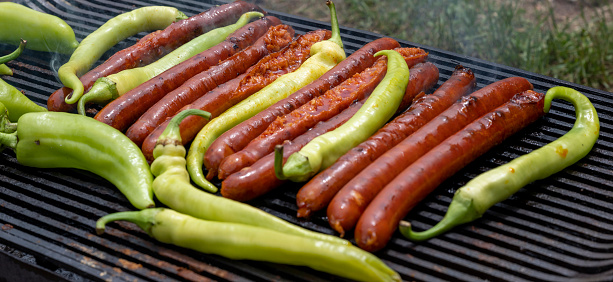 Green peppers and pork sausages on the barbecue grill. Fresh anaheim chili peppers roasting over a charcoal fire. Cooking peppers at the barbecue. Cayenne pepper.
