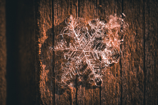 A macro shot of a snowflake on a wooden surface