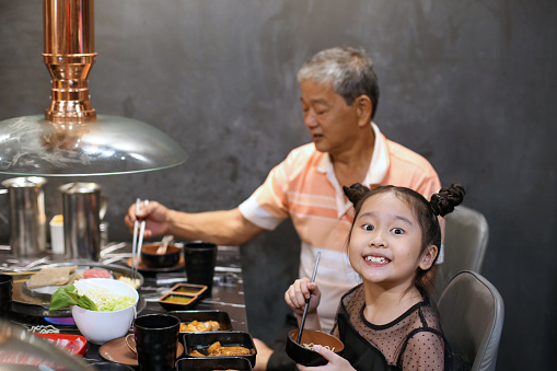 Asian family (grandfather and granddaughter) dining in restaurant for barbeque