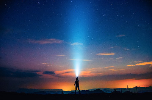 A person holding a flashlight under the starry sky