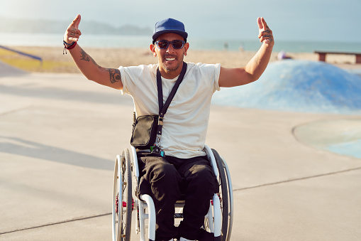 athlete man with disability in wheelchair smiling making hand gestures skatepark