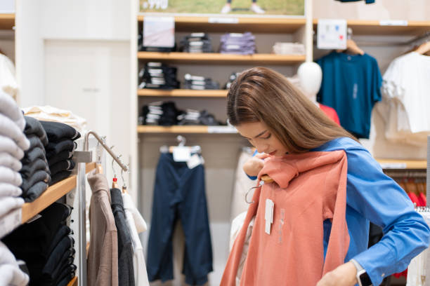 kaukasische oder brünette weiße frau mit braunen haaren beim einkaufen von kleidung, pullovern, hemden in einem kaufhaus. - shopping retail shirt coat hook stock-fotos und bilder