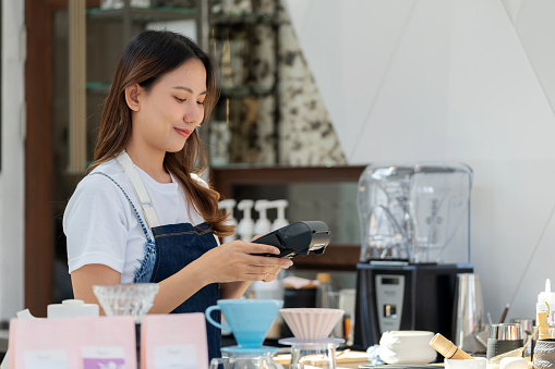 Seamless transactions as the young female owner of a coffee shop records payments for customers with precision and efficiency. Use of technology to facilitate secure and fast contactless payments. Small business owner embracing the future, providing customers with convenience and relaxation.