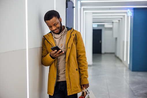 Smiling man typing message on smartphone after shopping