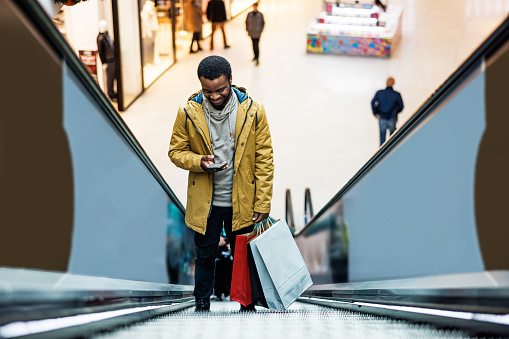 African American man using smartphone on escalator in shopping mall