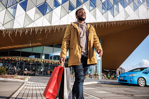 African American man walks with shopping bags after successful shopping