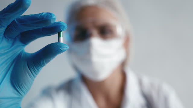 Laboratory assistant in protective clothing examining a pill, quality control