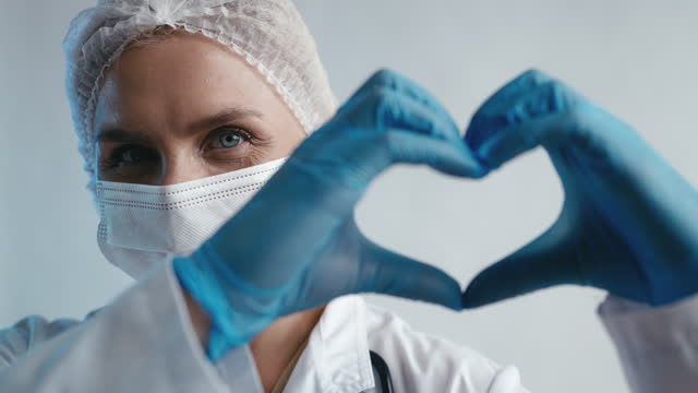 Friendly doctor in medical mask and gloves showing a heart gesture, profession