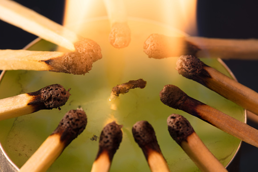 Close up of burning matches, all around a circular candle.