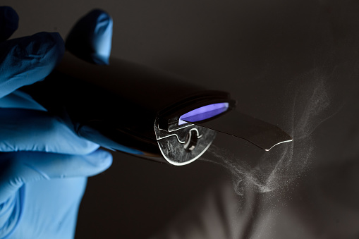 Cosmetologist's hand in a blue latex glove holds a switched on black ultrasonic scrubber on a dark background