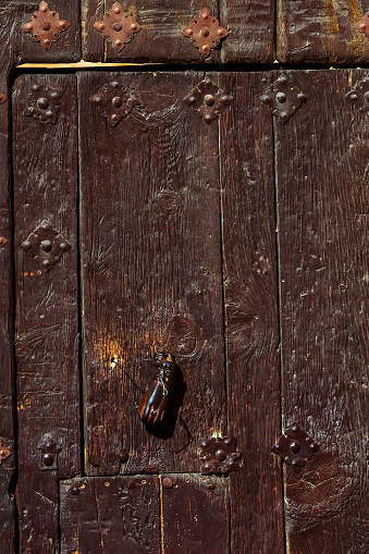 Dark wooden door adorned with iron studs and a vintage hand-shaped door knocker.