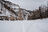 Frozen river, snowmobile tracks in the snow, mountainous terrain in winter, Russian winter, high cliffs above the river.