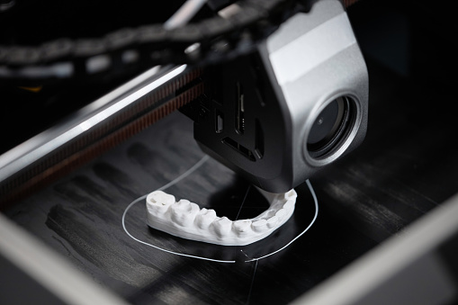 Macro shot of 3D printer extruder producing white-colored human lower jaw bone sample in engineering laboratory