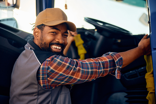 Happy African American truck driver getting into a vehicle and looking at camera.